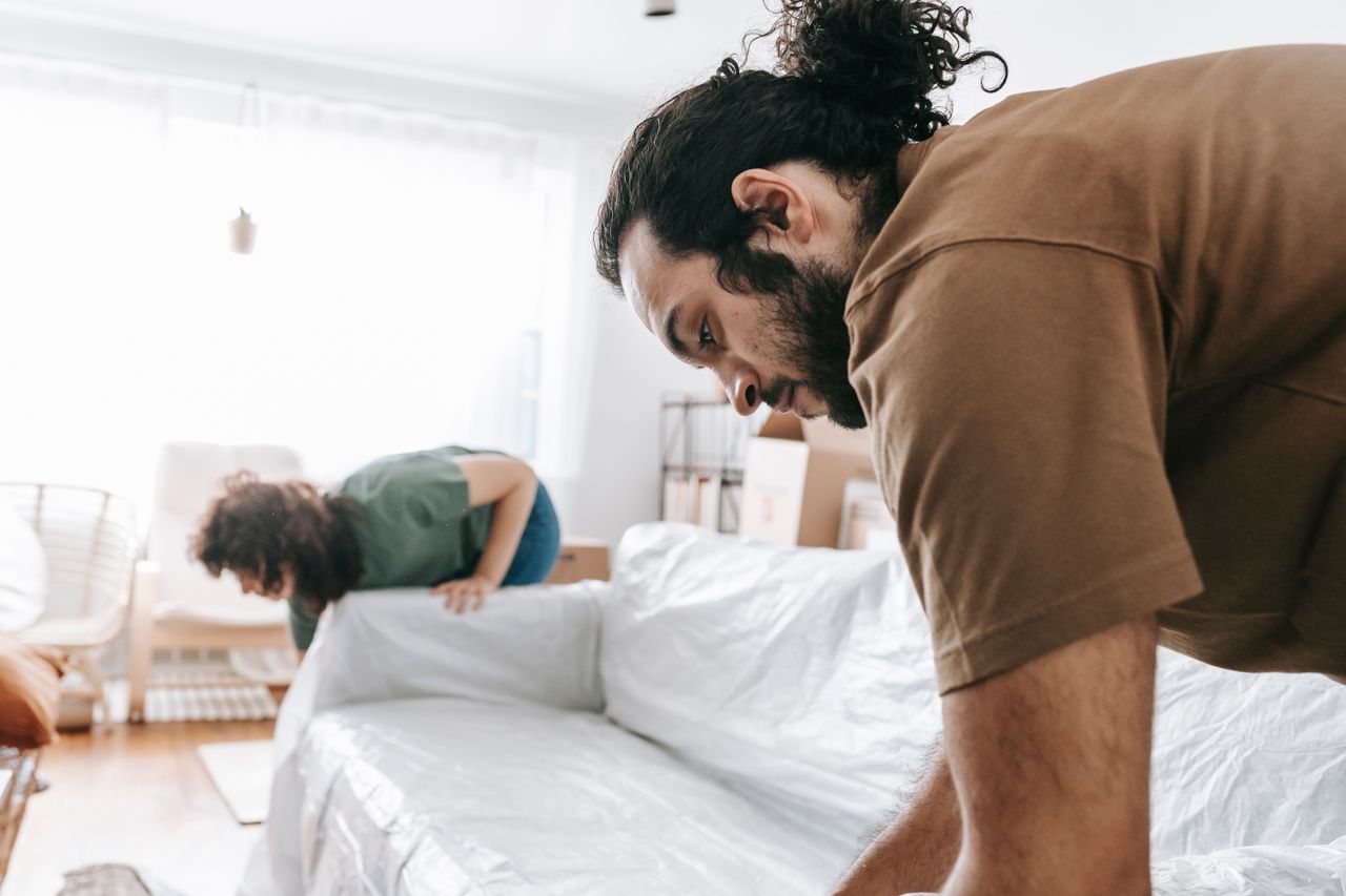A couple wrapping furniture in a bright apartment, getting ready to move.